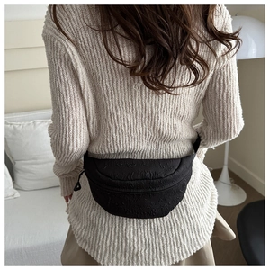 Detail shot of black pleated waist bag on model showing soft texture and zipper design