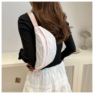 Close-up of white textured waist bag with pink woven strap on female model