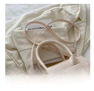Detail of minimalist beige faux crocodile embossed leather handbag with golden hardware