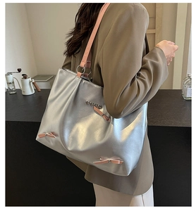 Close-up of silver tote bag featuring pink ribbons and metal heart charm on a shoulder strap