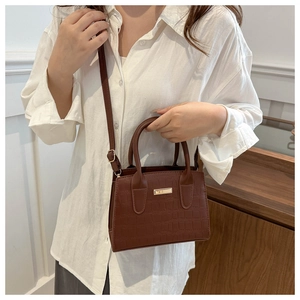 Detail of dark brown stone textured leather crossbody bag with gold plaque and top handles
