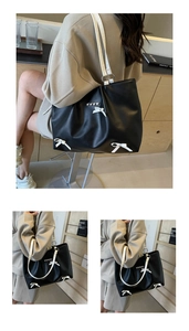 Detail of a large black tote bag with white bows and silver heart rivets worn by a model