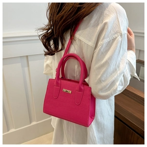 Close-up of rose red crocodile pattern handbag with golden metal bar and shoulder strap