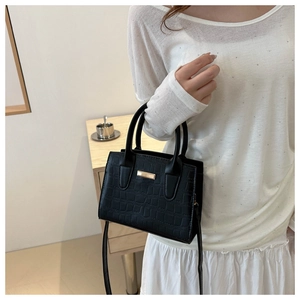 Detail of black crocodile texture handbag with gold metal bar and cylinder handles