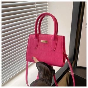 Detail of rose red crocodile embossed leather handbag with golden metal hardware