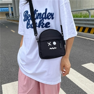 Minimalist black nylon crossbody bag with cartoon face on a model in urban street setting
