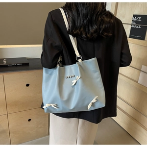 Detail of light blue tote bag with white bows and heart studs worn over the shoulder