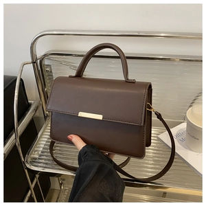 Détail d'un sac à main carré marron foncé avec boucle dorée sur un support minimaliste