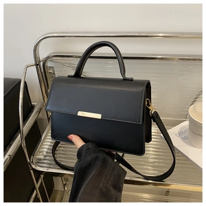 Détail du sac à rabat en cuir noir avec ferrures dorées et bandoulière réglable