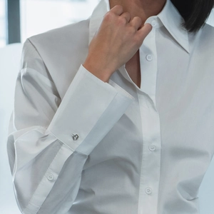 Détail d'une manche de chemise en coton blanc avec un bouton métallique géométrique au poignet