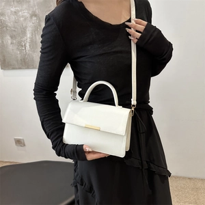 Sac à bandoulière minimaliste en cuir blanc crème avec boucle dorée porté par un mannequin