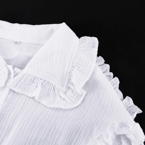 Détail macro du chemisier en coton blanc avec col à volants et tissu texturé, étiquette S