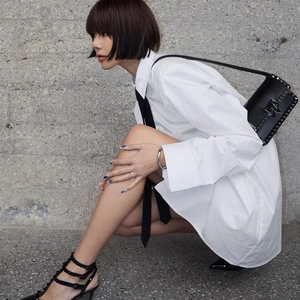 Donna in camicia bianca oversize e cravatta nera con sandali borchiati e borsa coordinata