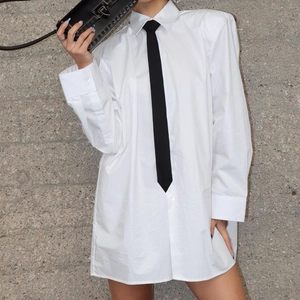 Dettaglio camicia bianca oversize in cotone con cravatta nera sottile e polsini abbottonati