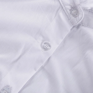 Dettaglio macro di camicia in cotone celeste con bottone a quattro fori e cuciture fini