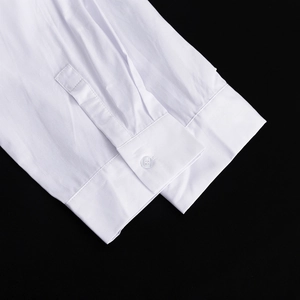 Dettaglio del polsino della camicia di cotone bianco con bottone su sfondo nero a contrasto