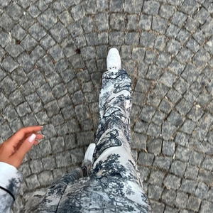 Detalle de pantalones satinados con estampado Toile de Jouy gris y mocasines blancos con hebilla