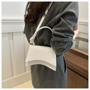Detail view of white crocodile pattern shoulder bag with a unique curved base and handle