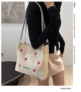 Detailed embroidery of red strawberries and fashion text on a woven straw tote bag