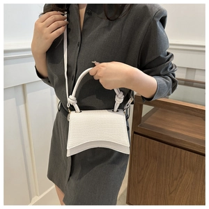 Detail of white crocodile embossed mini bag with curved base and knot handle accents