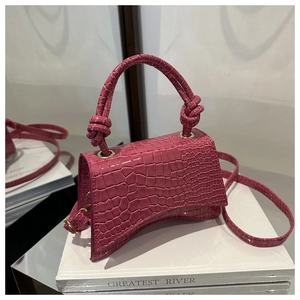 Detail shot of mini rose pink crocodile embossed handbag with curved base on white stand
