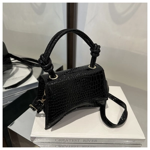 Detail of black crocodile pattern handbag with crescent curved base and knot handle
