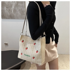Detail of straw woven tote bag featuring strawberry embroidery and double shoulder straps