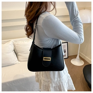 Detail of minimalist black leather tote bag with gold buckle on shoulder strap