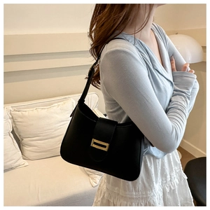 Detail of minimalist black hobo bag with gold buckle worn on shoulder by a model