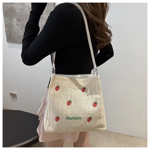 Detail of straw woven tote bag featuring red strawberry and fashion embroidery
