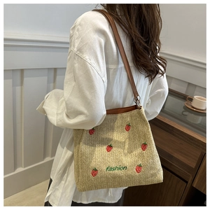 Detail of strawberry embroidery and fashion text on a woven straw tote shoulder bag