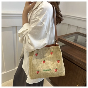 Close-up of beige straw bucket bag featuring red strawberry embroidery and fashion logo