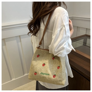 Detail of woven straw tote bag with strawberry embroidery and leather strap in soft lighting