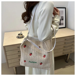 Detail of straw woven tote bag featuring embroidered strawberries and fashion lettering