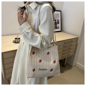 Close-up of beige woven tote bag with red strawberry embroidery and green fashion text