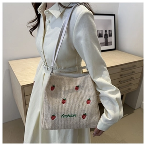 Detail of straw woven tote featuring strawberry embroidery and soft leather shoulder strap