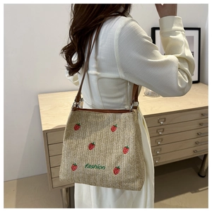 Detail of woven straw tote bag with strawberry embroidery and leather shoulder strap