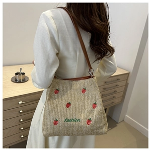 Detail view of woven tote bag featuring red strawberry embroidery and brown leather straps
