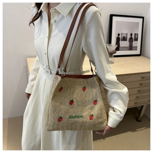 Close-up of straw woven tote with strawberry embroidery and brown leather straps