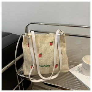 Detail of straw woven bucket bag featuring red strawberry embroidery and white strap