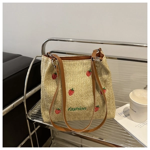 Close-up of strawberry embroidery and brown leather straps on a woven tote bag