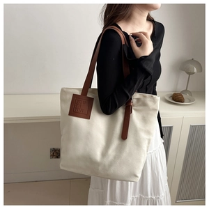 Detail of canvas tote bag with brown leather straps and adjustable buckle on model