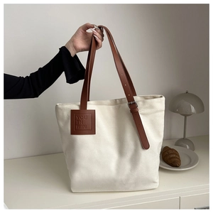 Detail of canvas tote bag showing brown leather straps and embossed logo patch