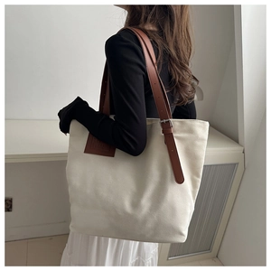 Canvas tote bag side view featuring adjustable brown leather straps and embossed patch