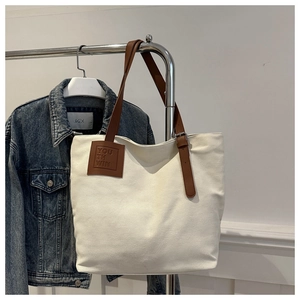Detail of canvas tote bag featuring brown leather straps and embossed square logo