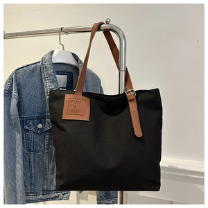 Detail of black canvas tote bag with brown leather straps and square logo patch