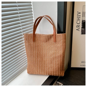 Detail of woven straw tote bag featuring herringbone pattern and brown leather handles