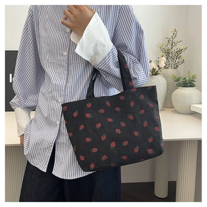 Détail du sac cabas en velours côtelé noir avec motif fraise rouge et tissu texturé