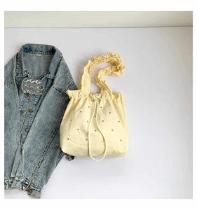 Detail of light yellow pleated tote bag with rhinestone studs and drawstring closure