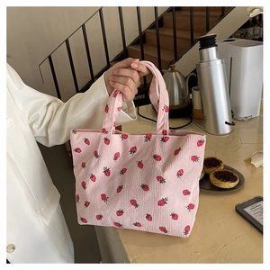 Detail of pink corduroy tote bag featuring fresh strawberry pattern in a cozy cafe setting